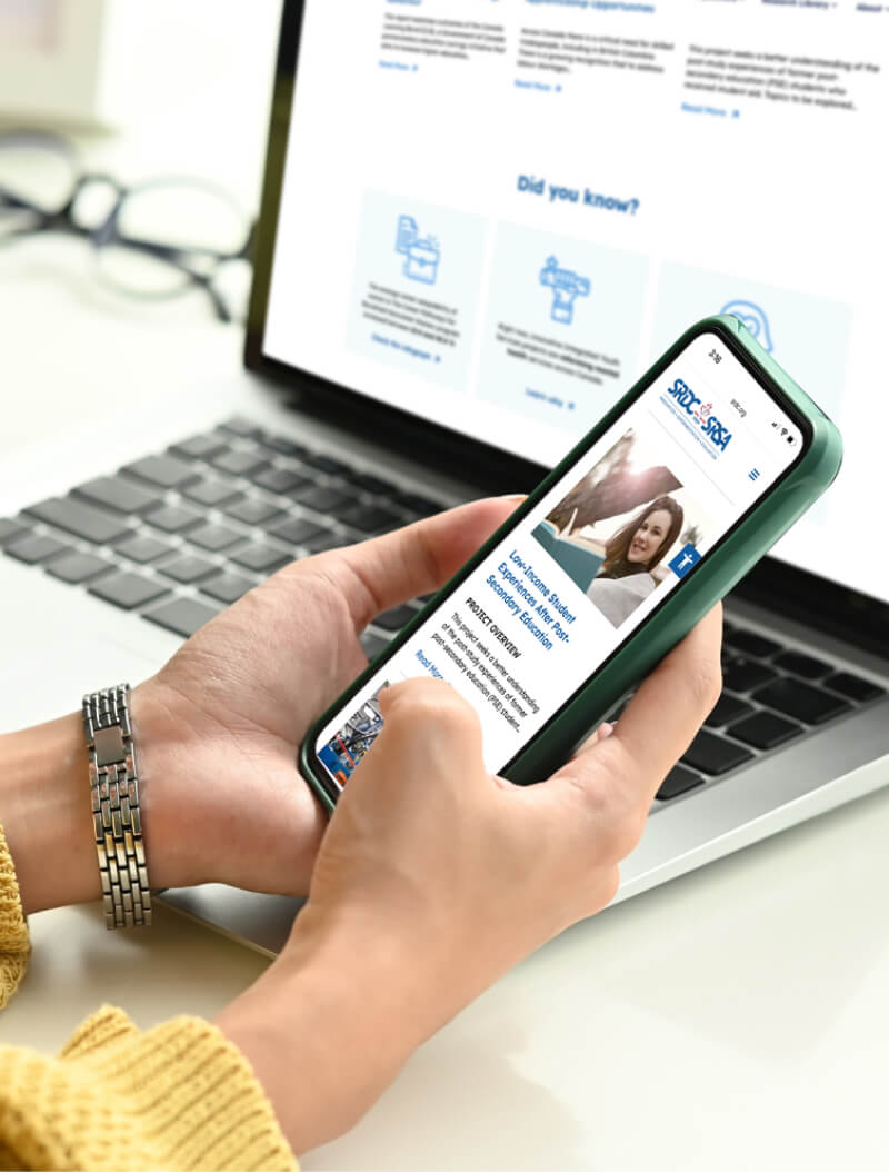A person browsing a website on a smartphone while working on a laptop.